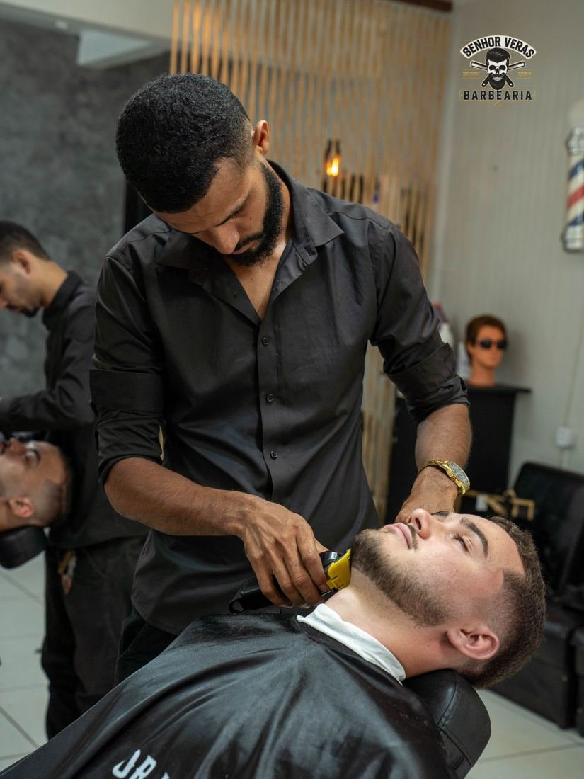 Barbeiro alinhando a barba de um cliente reclinado