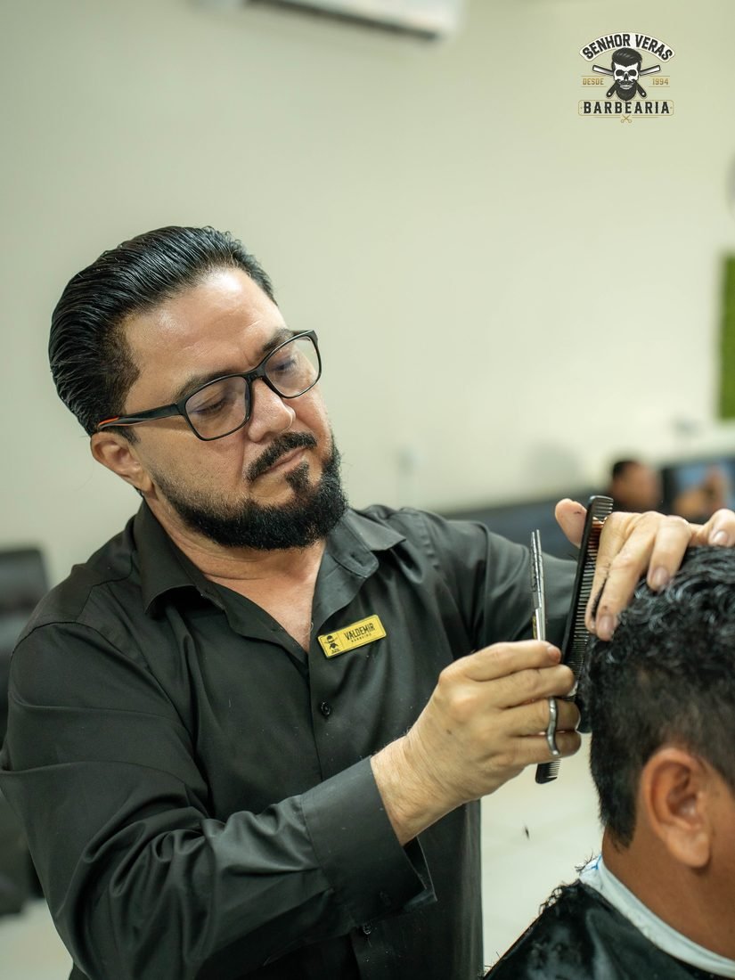 Veras cortando o cabelo de um cliente com pente e tesoura