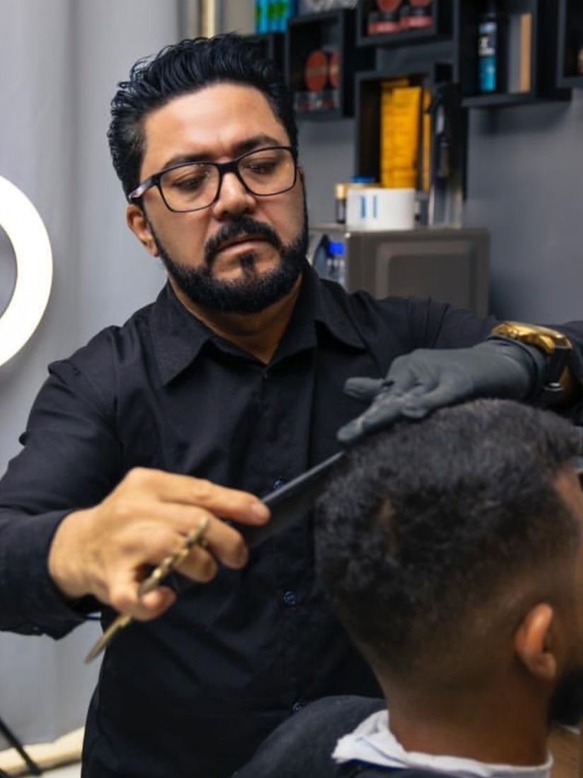 Veras cortando o cabelo de um cliente com pente e tesoura